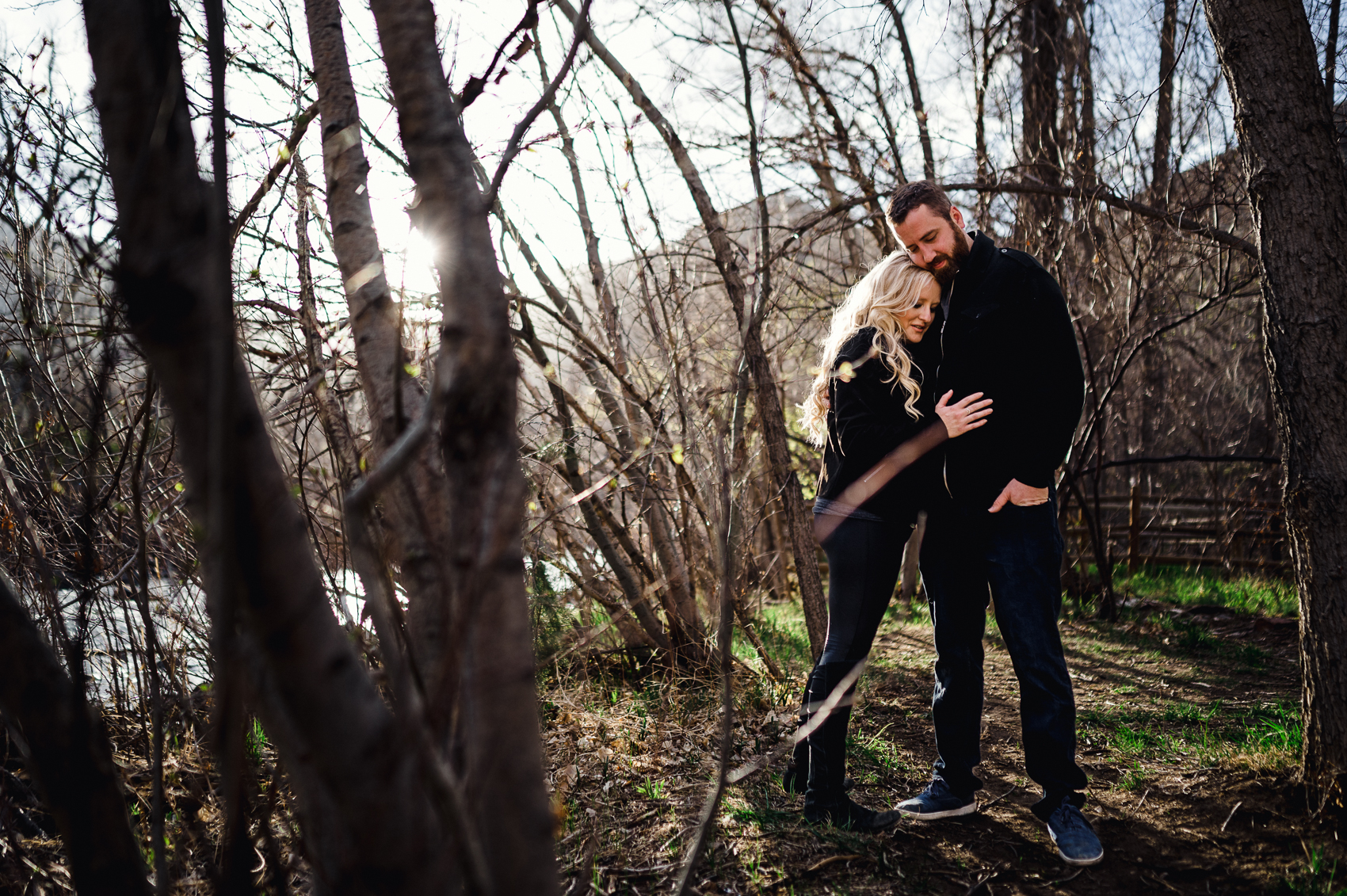 A couple laughing and snuggling for engagement photos next to Clear Creek in Golden, Colorado